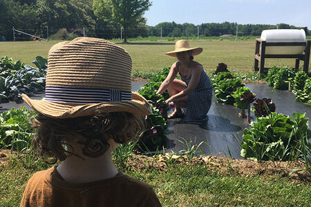 Woman plants in field. Small boy watches