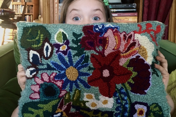 Small child holding a rectangle shaped punch needle pillow of various colours.